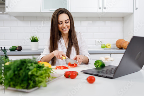 Принти на полотні Young cute brunette housewife cooking following the Internet recipes and cutting