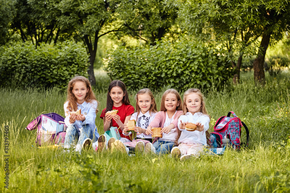 Obraz premium Young school kids eating lunch talking, together, sitting on the ground