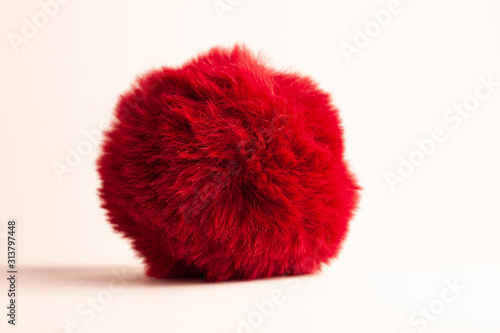 Red fur ball isolated on white background with natural shadow. Keychain, hats fashion style accessory, bag and backpack decoration. Girl clothes wardrobe,female style. Copy space.