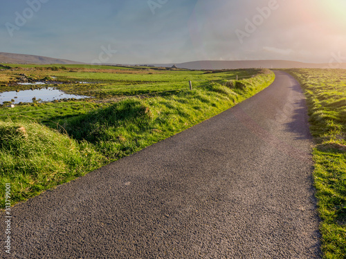 Small narrow country road without markings to a mountains, Nobody, clear sky, sun flare. Simple nature landscape.
