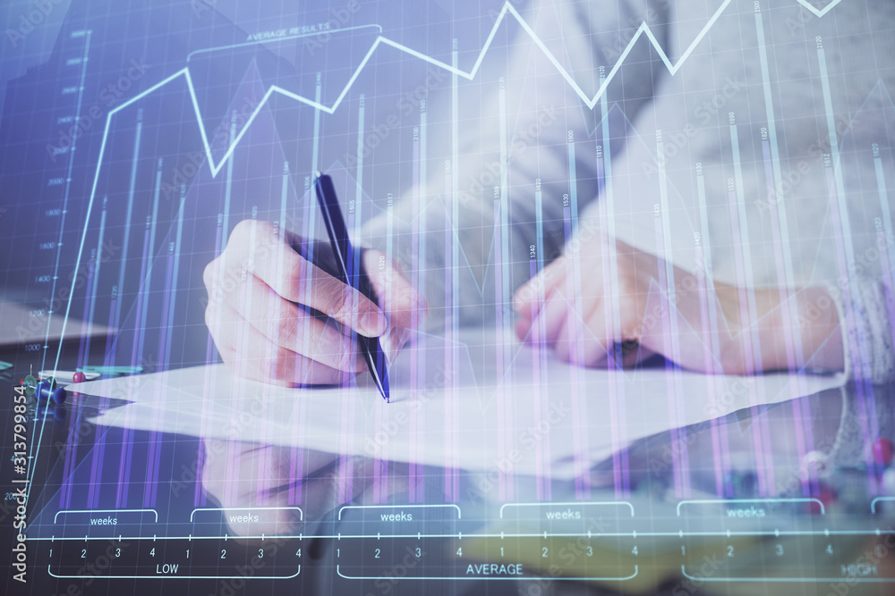 Hand taking notes in notepad. Forex chart holograms in front. Concept of research. Multi exposure Hand taking notes in notepad. Forex chart holograms in front. Concept of research. Multi exposure