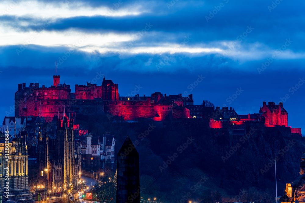 Edinburgh Castle illuminated red in the evening with a blue cloudy sky Scotland