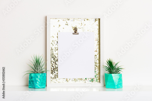 Lifestyle home decoration with frame and place for text. Marbled geometric succulent planters with beautiful tiny succulent plants on white shelf against white wall.