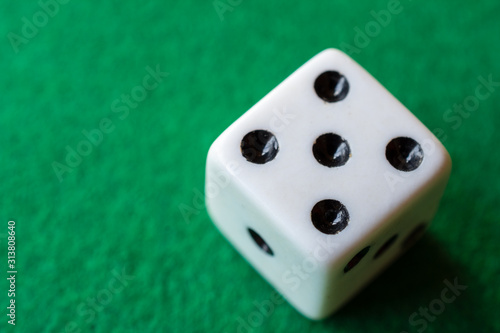 Top view in the foreground of dice with the number five, on green mat, horizontally with copy space