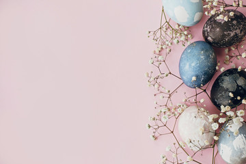 Stylish easter eggs and spring flowers border on pink paper flat lay, space for text. Modern natural dyed blue and marble easter eggs. Happy Easter. Greeting card template