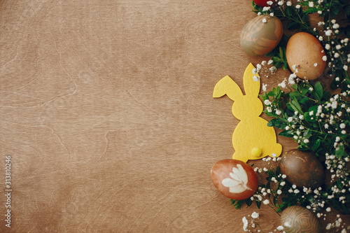 Happy Easter. Stylish easter eggs, yellow bunny, spring flowers on rustic wooden table flat lay, space for text. Natural dyed easter eggs and rabbit decorations on wood. Card mockup