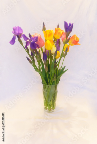 Bouquet of purple irises and yellow-pink tulips in a glass vase