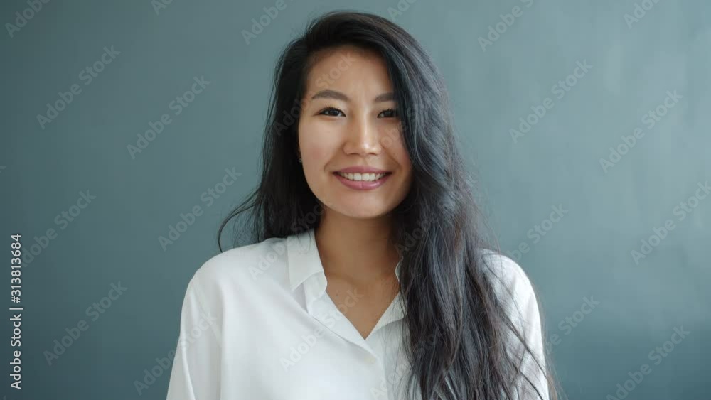 Slow motion of attractive young Asian woman smiling looking at camera standing alone on black background wearing elegant clothing. Youth and emotions concept. Slow motion of attractive young Asian woman smiling looking at camera standing alone on black background wearing elegant clothing. Youth and emotions concept.