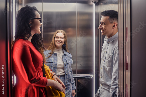 The girls and the guy ride in the elevator. Students in the elevator go to study. People in the elevator. Elevator with people, communication in public places. Colleagues go to work in the elevator.