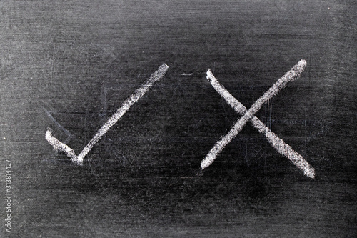 White color chalk hand drawing as check mark of right and wrong shape on black board background