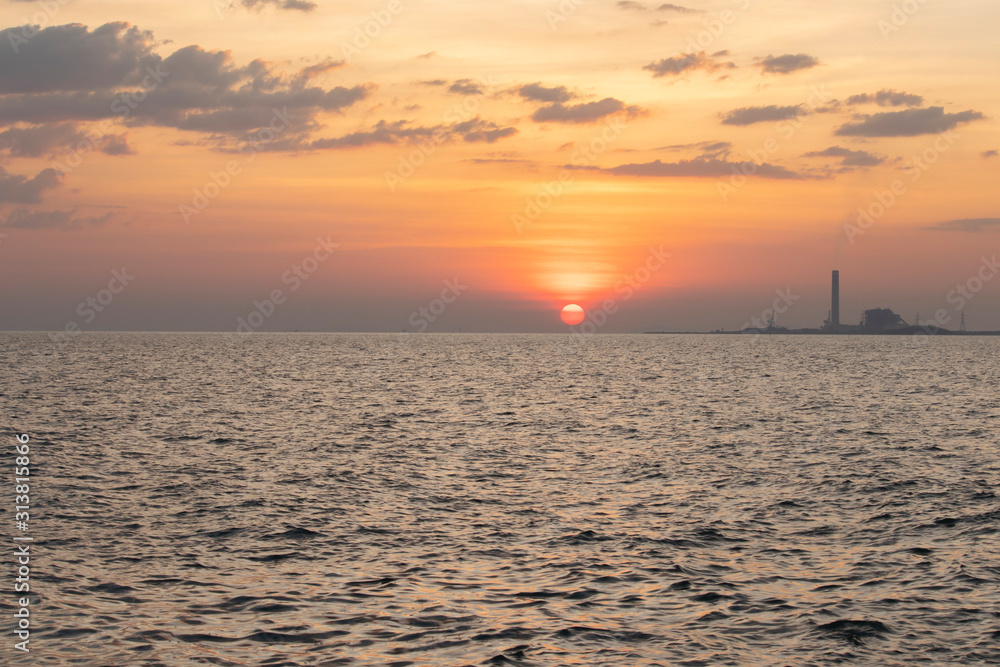 Fototapeta premium The red sun over the evening sea near the industrial area by the sea