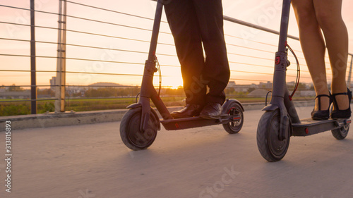 Εκτύπωση καμβά LENS FLARE: Co-workers in formal wear ride electric scooters to work at sunrise