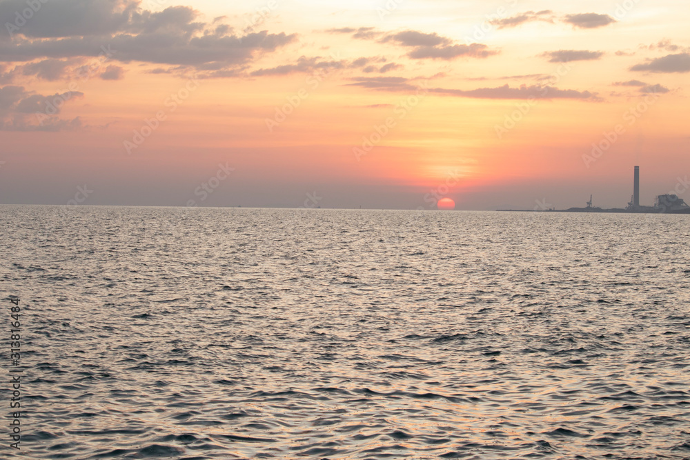 Obraz premium The red sun over the evening sea near the industrial area by the sea