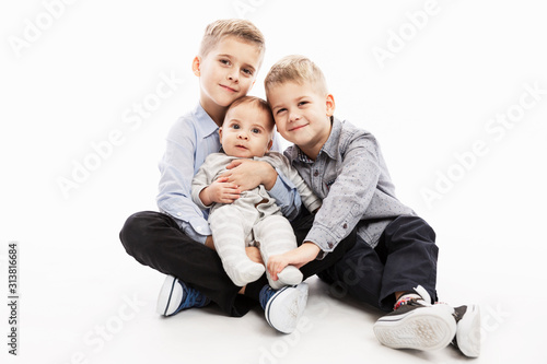 Two brothers are holding a newborn and smiling. Love and tenderness in the family. White background.