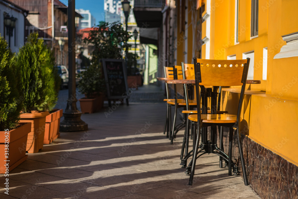 Naklejka premium Empty chairs of summer cafe standing outside on the street in historical part of touristic European city old center, Morning light.