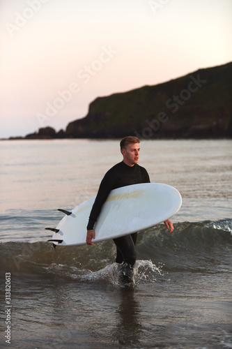 Photography Man Wearing Wetsuit Carrying Surfboard As He Walks Out Of Sea