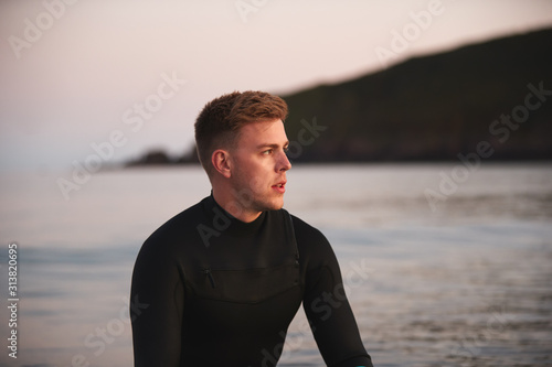 Man Wearing Wetsuit Sitting And Floating On Surfboard On Calm Sea