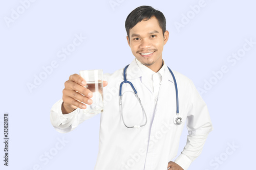 young man doctor with stethoscope standing and holding glass of water on purple background.