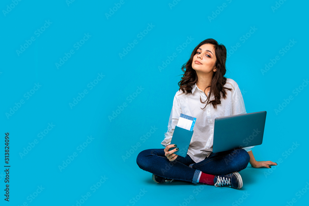 Naklejka premium Young woman sitting on the floor with laptop and passport buying tichets online