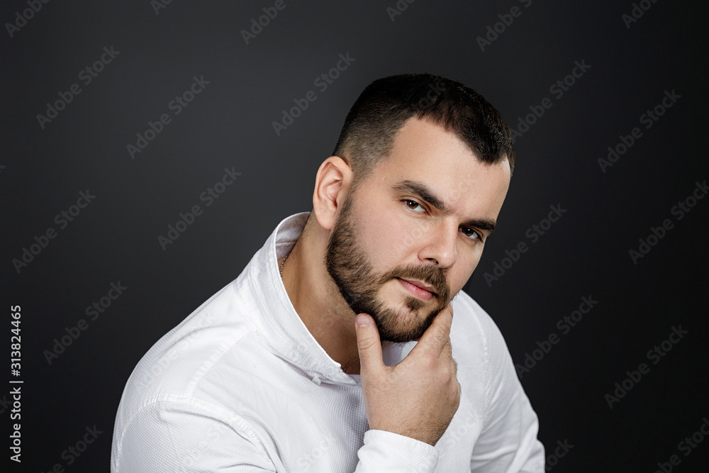man gazes steadily. Close-up portrait of handsome bearded man in white shirt looking at camera isolated on black background