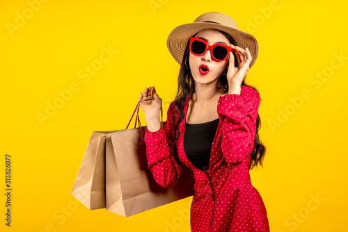 Asian trendy shopaholic woman excited about new purchases or sales holding shopping bags and looking to camera over yellow background. Happy beautiful Asian customer carrying shopping bags.