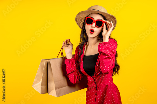 Foto Asian trendy shopaholic woman excited about new purchases or sales holding shopping bags and looking to camera over yellow background