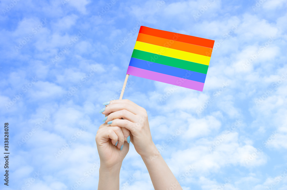 Fototapeta premium Flag LGTB in the hands of a caucasian woman against the sky with clouds.