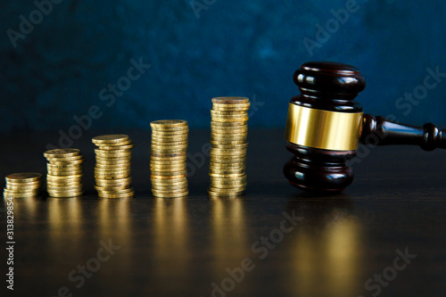 Close-up Of A Judge's Hand Holding Gavel Over Stacked Golden Coins
