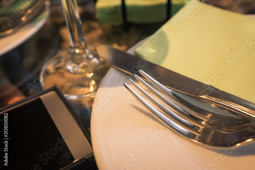 White plate with fork and knife and a green napkin on a glass table  with mobile phone and glass of wine