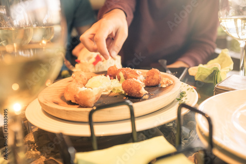 Caucasian man taking food, typical tapas from Spain, from a wooden plate and wine cups of glass ,during a meal celebration with friends. Soft sunlight entering from the side