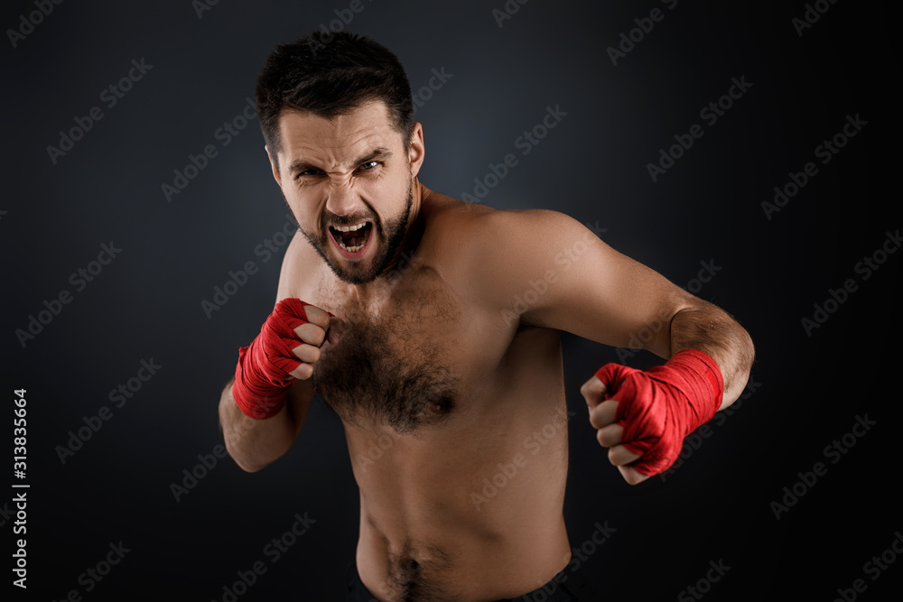 Sportsman boxer throwing a fierce and powerful punch. muscular man with red bandage on hands on black background.