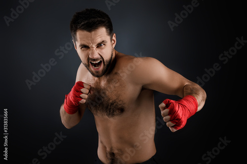 Sportsman boxer throwing a fierce and powerful punch. muscular man with red bandage on hands on black background. © producer