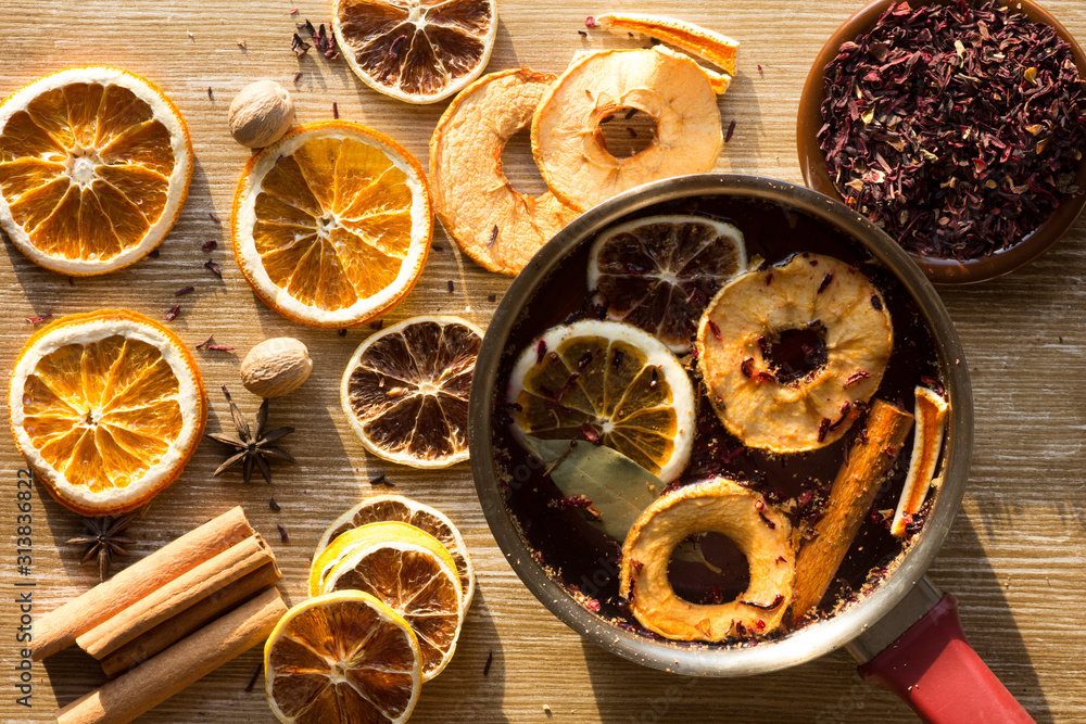 Top view of dry pieces of lemon, orange and apple, cinnamon sticks, bay leaves, nutmegs, star anise and dry cutted hibiscus and the saucepan with water and ingredients in it Top view of dry pieces of lemon, orange and apple, cinnamon sticks, bay leaves, nutmegs, star anise and dry cutted hibiscus and the saucepan with water and ingredients in it