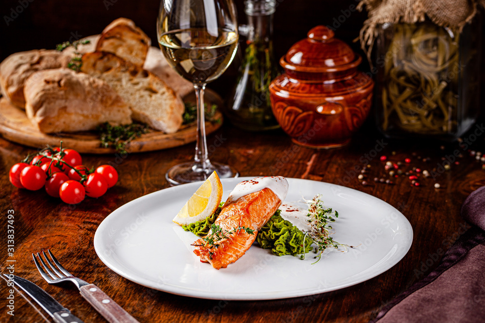 Italian Cuisine. Red fish steak, salmon with lemon, a side dish of spinach. Beautiful restaurant serving in a white plate with a glass of white wine. background image, copy space