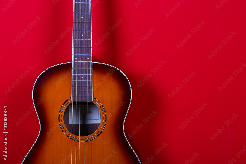 Cropped image of vintage style travel size acoustic guitar with rosewood neck and no pickguard over festive red wall background. Close up, copy space for text, top view.