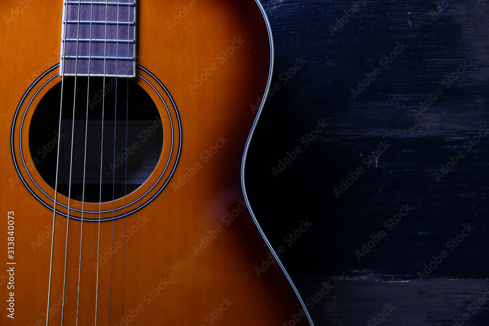 Obraz premium Cropped image of vintage style travel size acoustic guitar with rosewood neck and no pickguard on grunged dark wood textured background. Close up, copy space for text, top view.