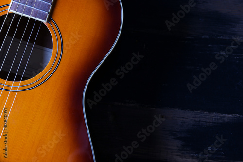 Cropped image of vintage style travel size acoustic guitar with rosewood neck and no pickguard on grunged dark wood textured background. Close up, copy space for text, top view.