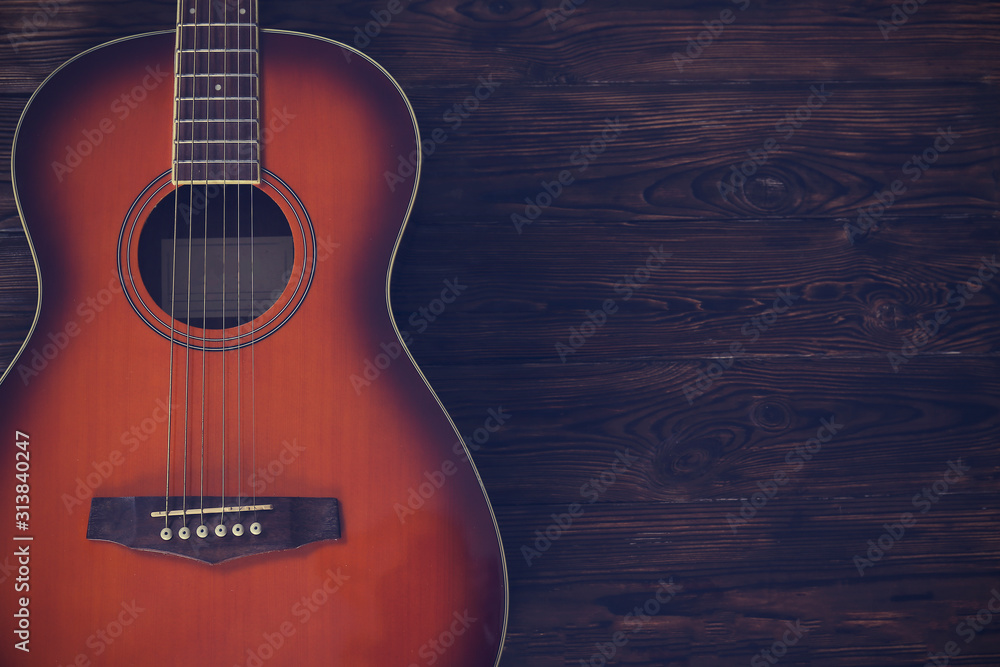 Fototapeta premium Cropped image of vintage style travel size acoustic guitar with rosewood neck and no pickguard on grunged dark wood textured background. Close up, copy space for text, top view.