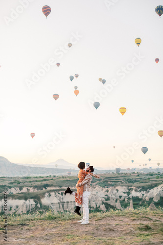 Woman and man watching colorful hot air balloons flying over the valley at Cappadocia, Turkey.Turkey Cappadocia fairytale scenery of mountains. Turkey Cappadocia fairytale scenery of mountains