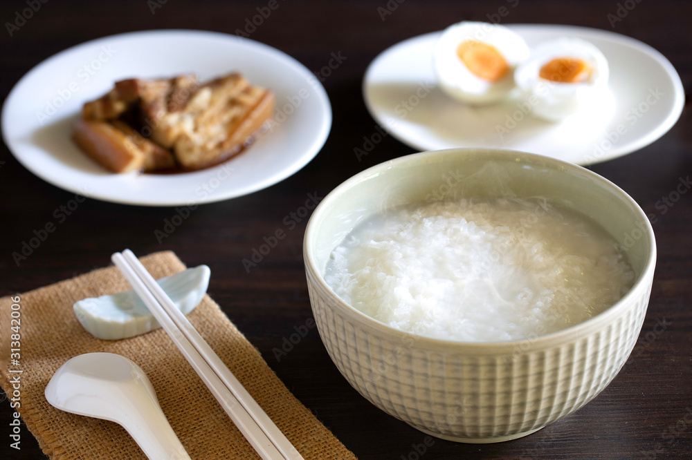 Boiled rice in gray bowl with food for eating which has chopstick with spoon all put  on dark wooden table
