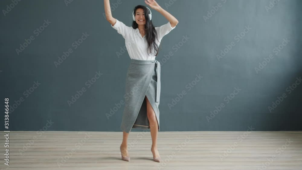 Cute Asian girl millennial is dancing in studio on dark gray background wearing headphones having fun alone enjoying activity. Modern people and devices concept. Cute Asian girl millennial is dancing in studio on dark gray background wearing headphones having fun alone enjoying activity. Modern people and devices concept.