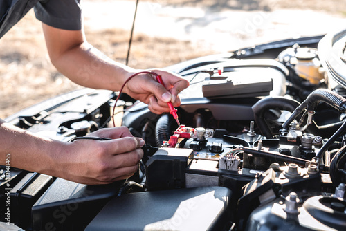 Mechanic repairman checking engine automotive in auto repair service and using digital multimeter testing battery to measure various values and analyze