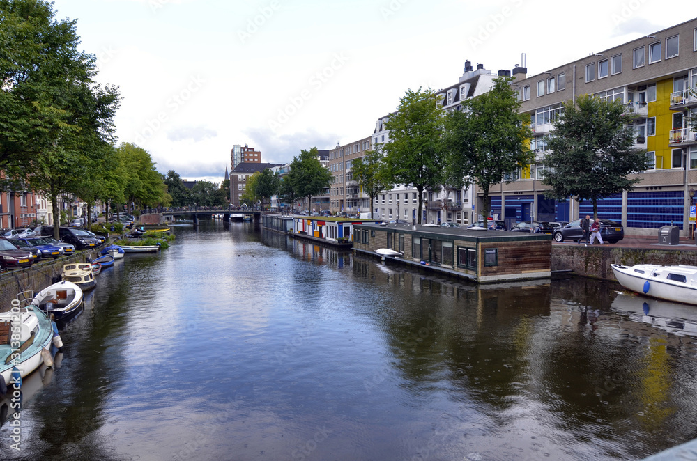 Amsterdam,Holland,August 2019. In the historic center a view that is a symbol of the city: a brown houseboat moored on the edge of the canal. Behind it the tree-lined avenue and the little houses