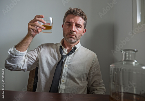 portrait of 30s to 40s alcoholic  man in lose necktie drinking desperate holding whiskey glass thoughtful drunk and depressed completely wasted in alcohol addiction concept photo