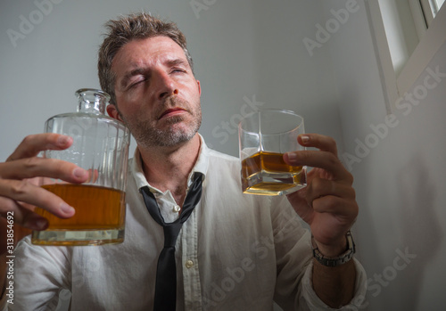 portrait of 30s to 40s alcoholic  man in lose necktie drinking desperate holding whiskey glass thoughtful drunk and depressed completely wasted in alcohol addiction concept