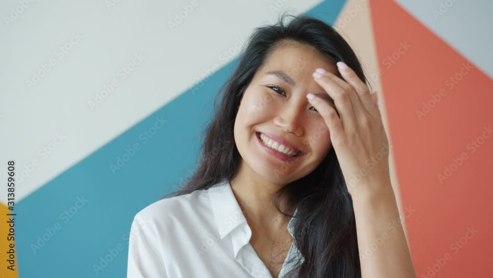 Attractive Asian female adult is smiling laughing at home on colorful background standing alone looking at camera, positive emotions and lifestyle concept.