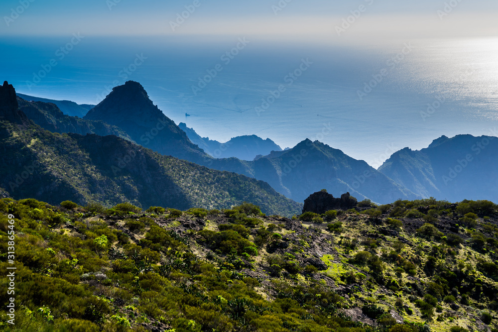 Spain, Tenerife, Wide view over blue ocean horizon and boats from cliffy green mountains of masca canyon on sunny day