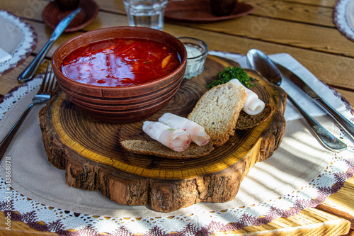 Beet soup in ceramic plate with becon, bread and sour cream on wooden board. Borch, traditional Ukrainian food photo