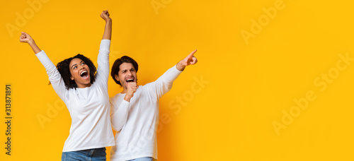 Multiracial couple dancing and singing together, having fun over yellow background photo