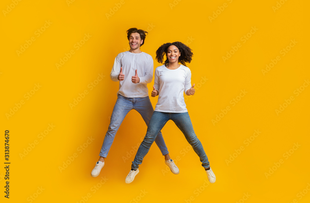 Joyful Interracial Couple Jumping In The Air And Showing Thumbs Up